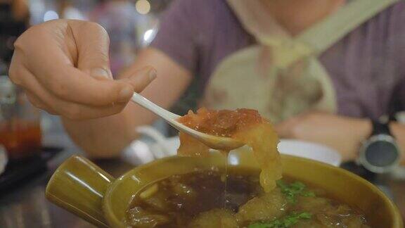 在曼谷唐人街耀拉瓦的一家街头小吃店在金属桌子上用塑料勺盛着热腾腾的鱼肚汤用美味的食物跟随手