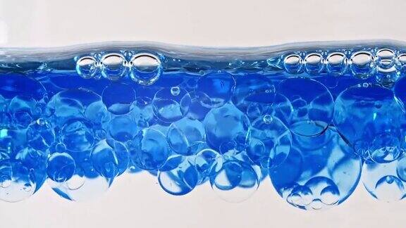 微距拍摄的各种气泡在水中上升在浅白色背景清澈的蓝色水中有气泡矿泉水富氧水慢动作