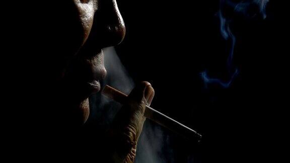 一名男子在黑色背景下吸烟的慢镜头