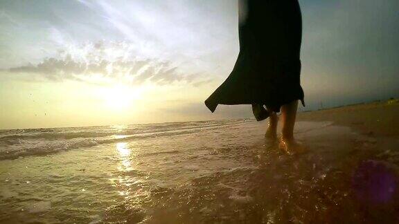 女人走在沙滩和水在日落