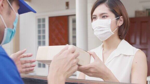 亚洲快递员戴口罩为亚洲女性客户送包裹新常态配送理念