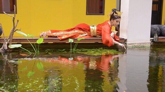 身着红旗袍的女子在池塘边休息