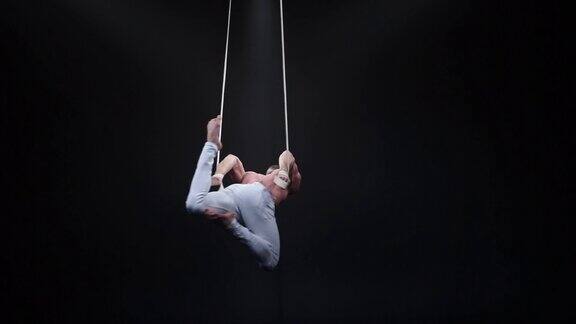 在黑色演播室的空中吊带上的肌肉发达的马戏团杂技演员
