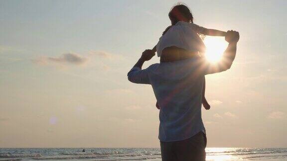 女儿骑在父亲的肩膀上在海滩上度假/幸福的家庭