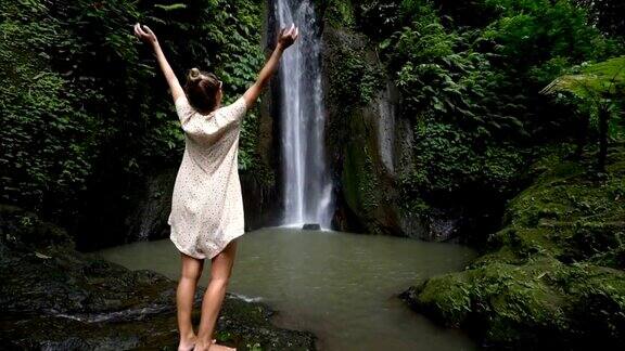 慢动作年轻女子享受新鲜瀑布在巴厘岛印度尼西亚亚洲人们旅游乐趣自然女孩伸着胳膊