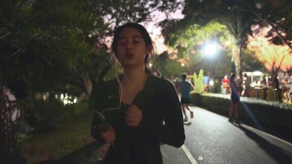 迷人的亚洲少女听音乐同时在公园里跑步年轻女子在晚上慢跑锻炼