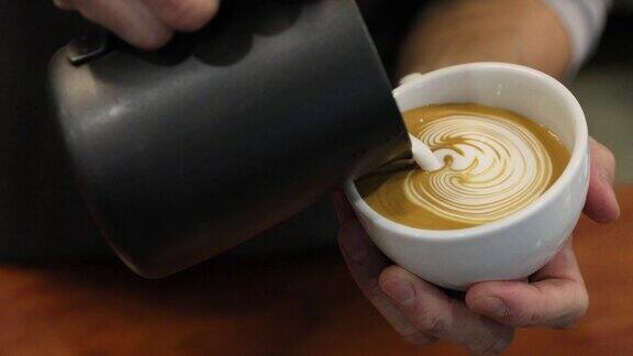 专业的咖啡师将蒸牛奶倒入白色的咖啡杯中制作美丽的罗塞塔拉花图案