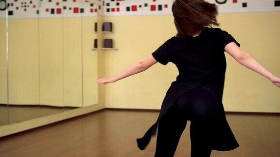 一个穿着黑衣服的职业舞蹈女孩在一个大的训练大厅里跳舞