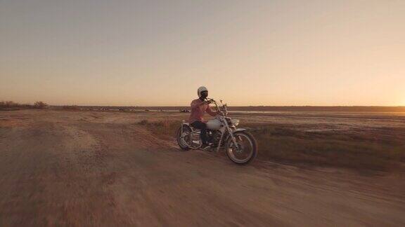 年轻时尚的摩托车手驾驶他的摩托车在沙漠道路在日落