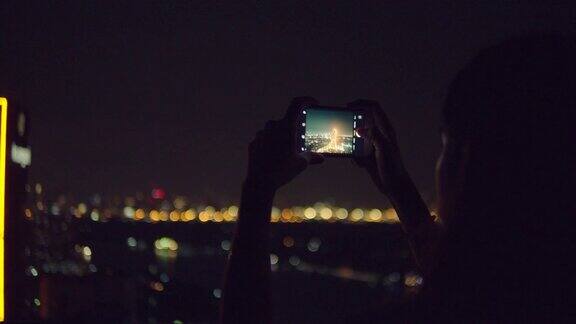 年轻的亚洲女人在晚上的城市里用美丽的散景用智能手机