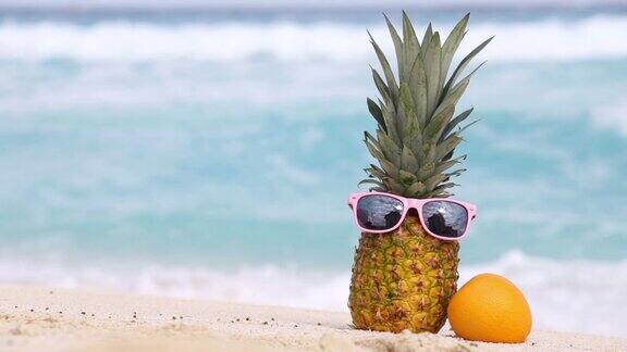 戴着墨镜的菠萝和沙滩上的橙色水果映衬着加勒比海的绿松石海水