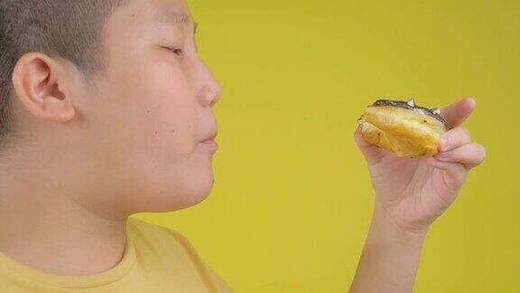 肥胖的亚洲十来岁的男孩吃黄色背景的甜甜圈