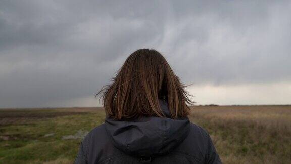 女人站在草地上望着地平线和黑暗中戏剧性的乌云后视镜