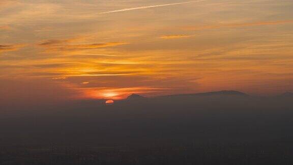 太阳落在低云后面的山的剪影美丽的橙色天空太阳和云的运动白天到夜晚的过渡-4k延时视频