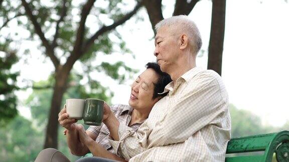 慢镜头亚洲退休夫妇谈论和喝咖啡早上在户外公园