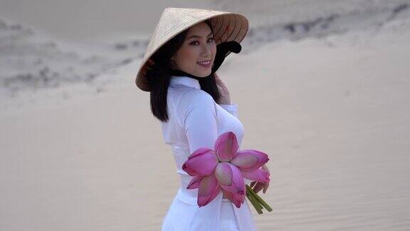 美丽的越南人捧着粉红莲花在白色沙丘沙漠上行走的4K电影越南
