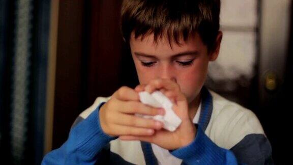 一个生病的男孩坐在家里的桌子上用餐巾擤鼻涕