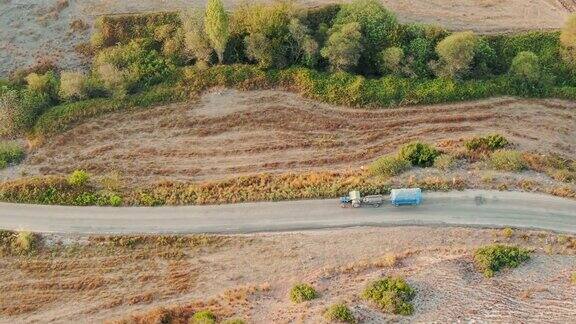 鸟瞰图在非农村田地之间的乡村道路上驾驶拖拉机和拖车早晨日出之光