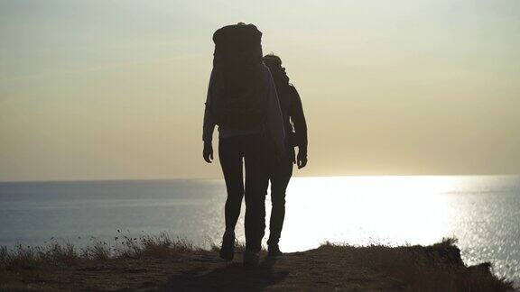 两个背着背包的游客在山顶上背对着海景行走
