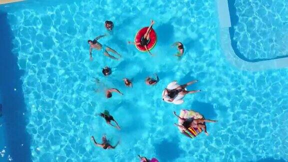 朋友们在游泳池里用充气火烈鸟天鹅床垫开派对的航拍阳光灿烂的日子里快乐的年轻人在豪华的度假胜地放松从以上观点穿着比基尼的女孩在阳光下晒日光浴