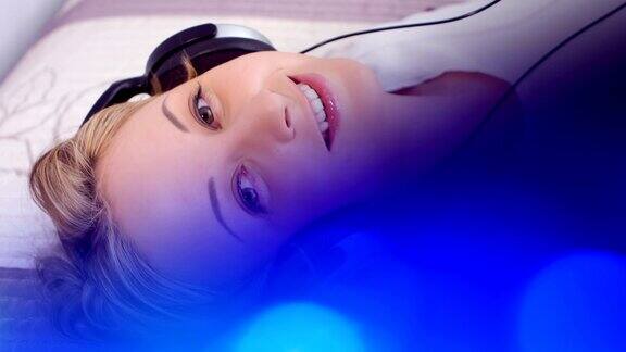 漂亮女孩戴着耳机和蓝色背景听音乐