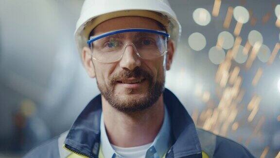 身穿安全制服、护目镜和安全帽的专业重工业工程师工人的微笑肖像背景中未聚焦的大型工业工厂焊接火花飞扬