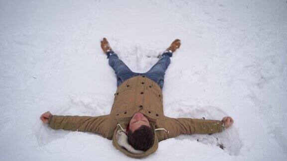 一个年轻人的肖像穿着夹克和牛仔裤躺在雪地里英俊的男人说谎摊开双手闭上眼睛在冬季公园的乐趣松软的雪包裹着周围的一切