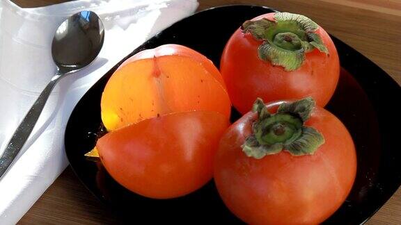 黑盘子上放着成熟的橙柿子