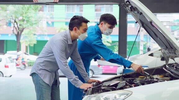 亚洲汽车技师听客户解释汽车状况在新冠肺炎疫情期间车辆服务经理戴着口罩在修车厂维修汽车发动机