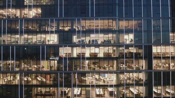 无人机拍摄的摩天大楼办公室在夜间的摄像头放大办公室的窗户人们在他们的电脑上工作到很晚