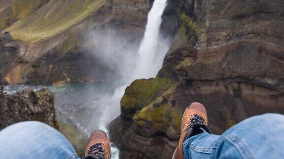 人的视角坐在悬崖上看着峡谷中的瀑布