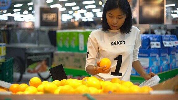 年轻的亚洲女人在杂货店挑选橙子