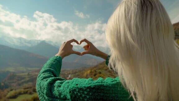 在山顶上徒步旅行的女子用她的双手制作了心形的手指框