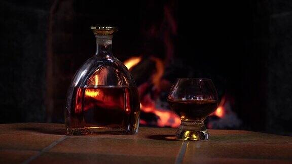 酒瓶和玻璃杯威士忌或干邑白兰地在壁炉的火的背景