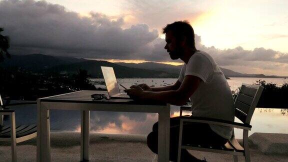 商人在室外阳台上用笔记本工作可以看到傍晚的海