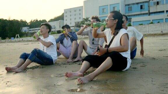 年轻的亚洲成年人坐在海滩上放松喝着啤酒敬酒