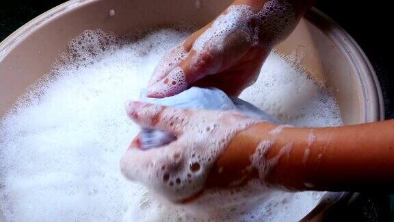 女性手在盆里洗衣服用洗涤剂手洗脏衣服上的污渍4k运动镜头