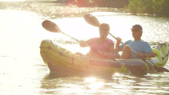 慢镜头:一对快乐的夫妇在假期中享受夏日日落在美丽平静的水面上划独木舟