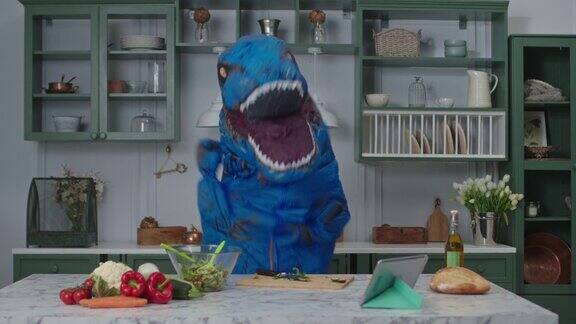 蓝色的大恐龙切好食物开始在厨房里跳舞滑稽动作的人在恐龙吉祥物在家保持积极的情绪愉快地烹饪