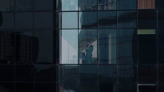 鸟瞰图镜头:从外面到办公大楼商人在用手机站在办公室窗户旁边美丽的飞走的金融商业区摩天大楼