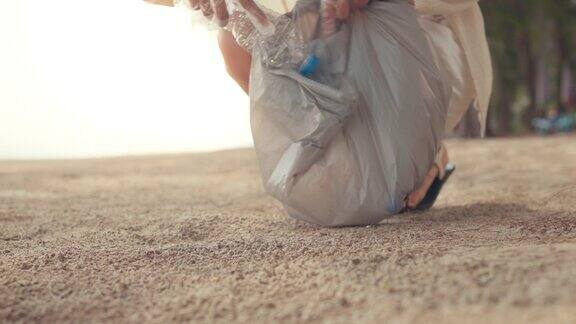年轻的旅游妇女将塑料瓶装入垃圾袋用于清洁海滩生态概念和世界环境日拯救地球