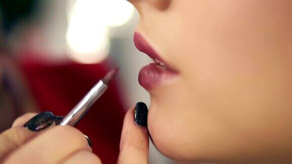 一个专业的化妆师的手使用特殊的刷子应用口红的模特的嘴唇在美容时尚行业工作的特写视图Slowmotion拍摄