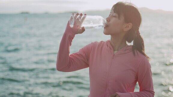 女跑步者站在海边喝水