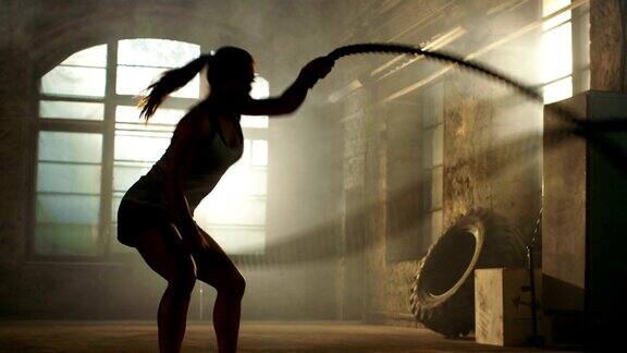 强壮的女运动员练习与战斗绳索作为她的健身健身房锻炼的一部分她满身的汗水和训练发生在一个废弃的工厂改造成健身房