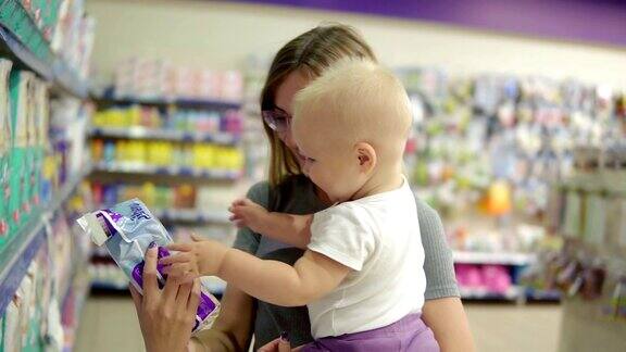 微笑的妈妈在超市的儿童区抱着她的孩子在超市货架上为她的孩子选择最好的产品尿布