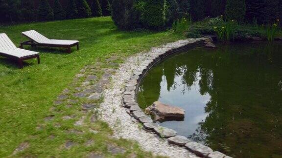 在一个美丽的花园中后院靠近池塘的躺椅上草地上有两张空的日光浴床