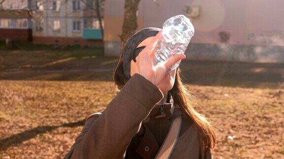 戴着太阳眼镜的黑发女子在街上喝瓶子里的水打开瓶子喝水然后关上瓶子