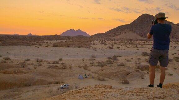 非洲纳米比亚男摄影师拿着相机看着风景优美的斯匹茨科佩山峰