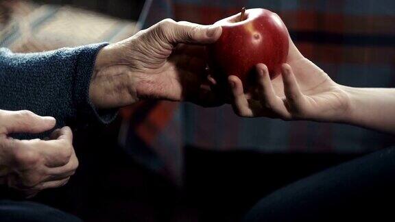 一个老妇人把一个红苹果递到一个十几岁的孩子手里