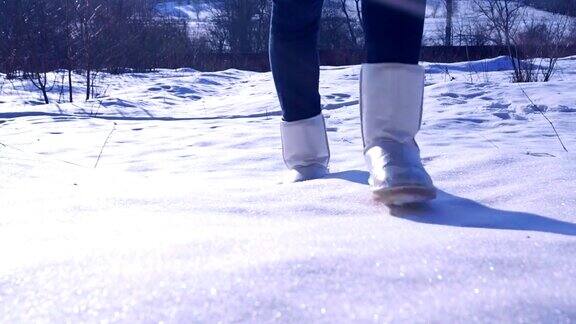 女孩穿着银色冬靴走在阳光明媚的雪地上缩小慢动作视频